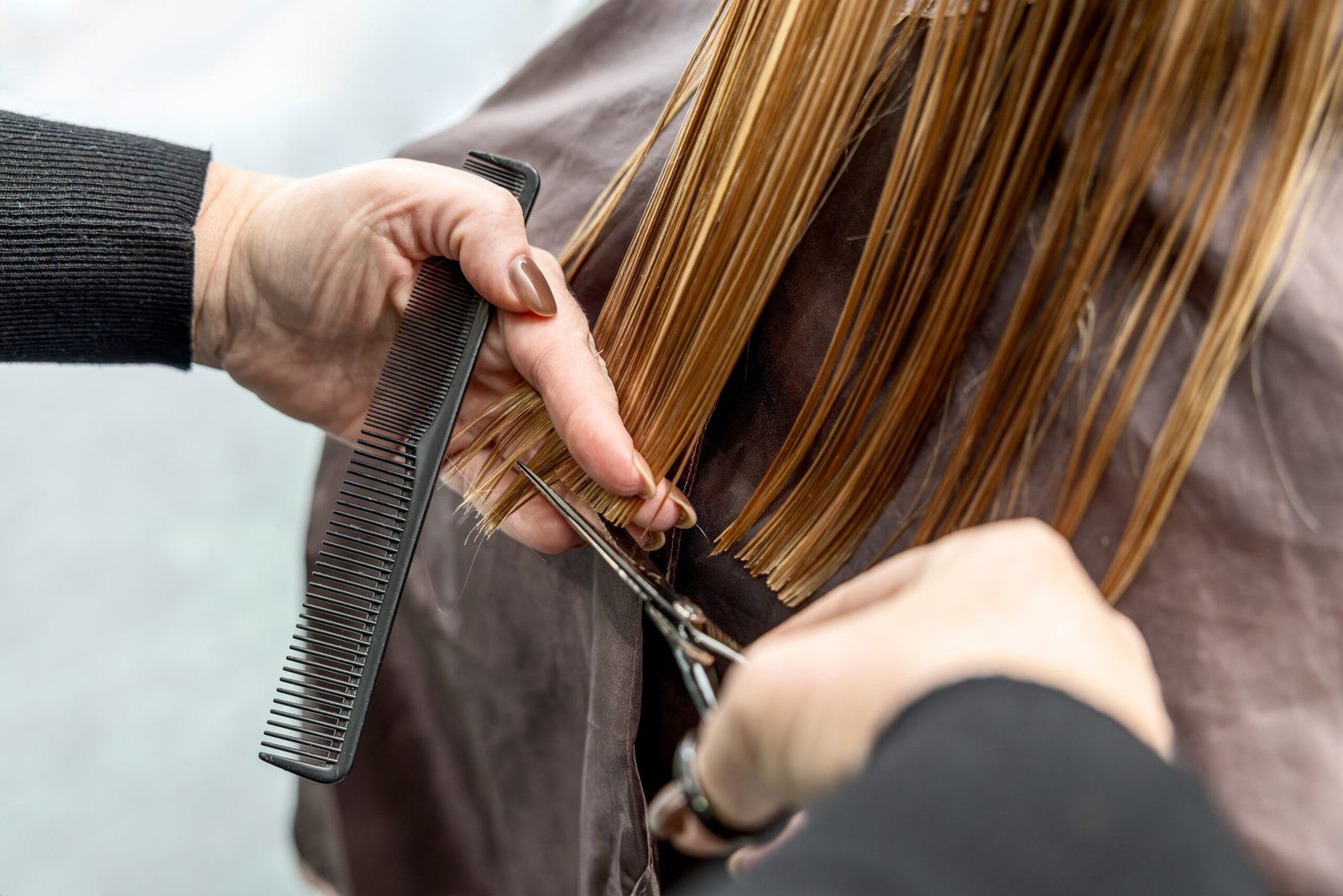 Close-up of hairdresser cutting straight wet hair with scissors and comb