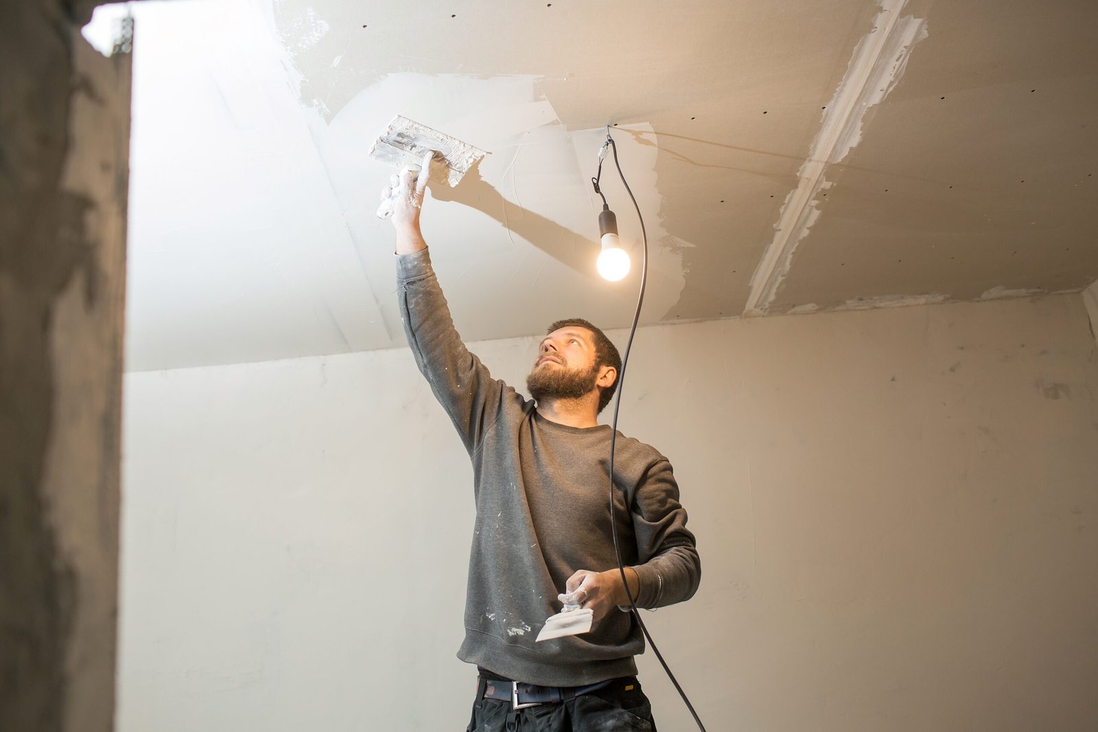 a man with a beard plasterer plasters the ceiling in a room with a spatula